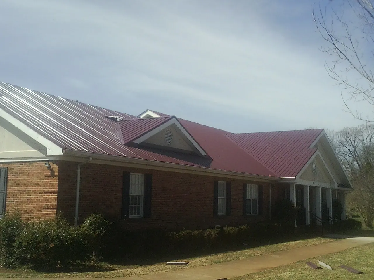 Red metal roof with gabled entries on a long brick building, from a Hail Damage Roof Repair job in Powell